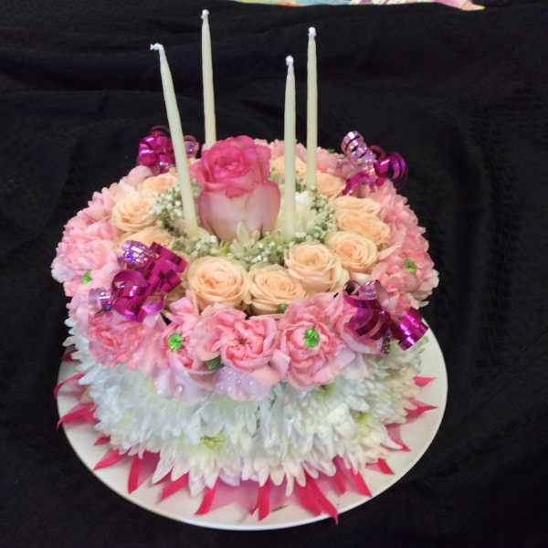 Round floral cake with pink and peach roses and four white candles