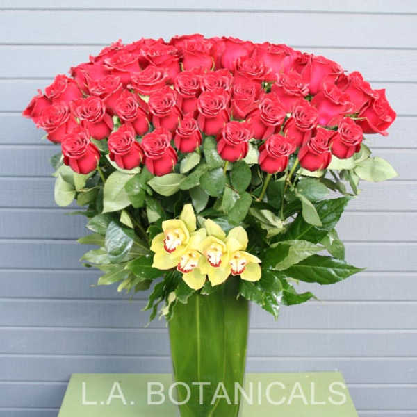 Tall bouquet of red roses with yellow orchids in a glass vase