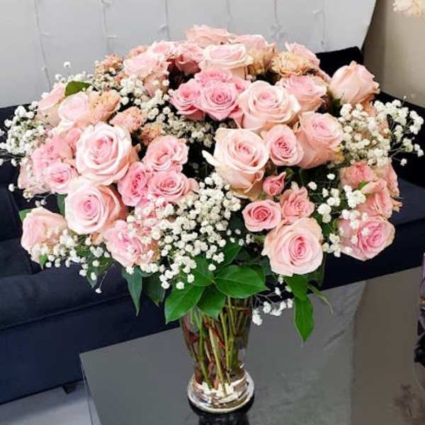 Large arrangement of pink roses and white filler flowers in a clear glass vase.