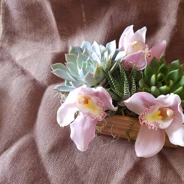 Succulent arrangement with pink orchid blooms in a wooden container