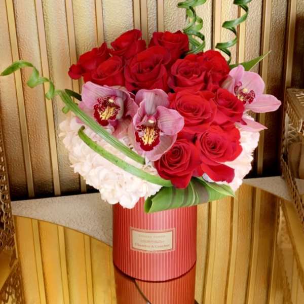Red roses and pink orchids arranged in a striped hatbox