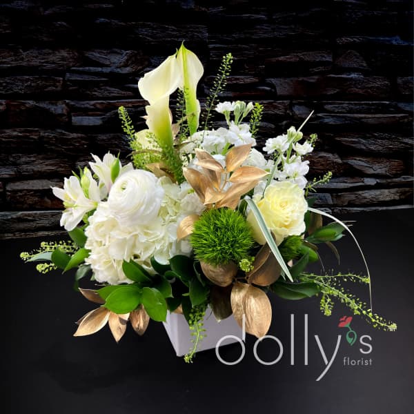 White floral arrangement with calla lilies, roses, and hydrangeas in a white container