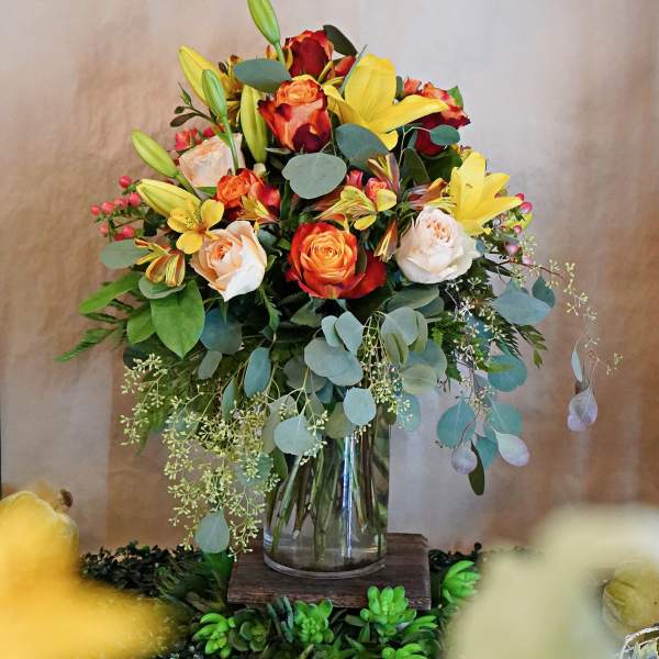Tall bouquet of orange roses and yellow lilies with cream roses in a clear glass vase