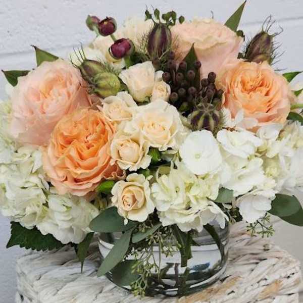 Low arrangement of peach and cream roses with white hydrangeas in a clear glass vase.