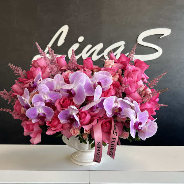 Pink roses and lavender orchids in a white pedestal vase