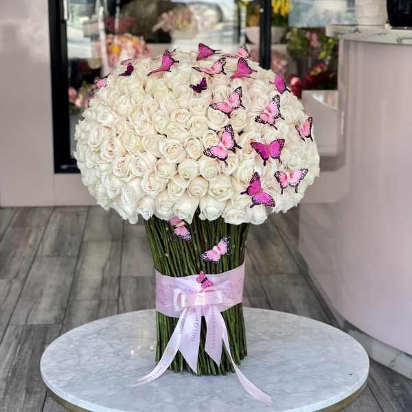 Large bouquet of white roses with pink butterfly accents and a pink ribbon