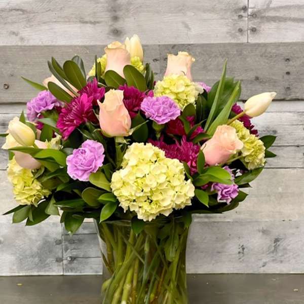 Mixed bouquet of roses, hydrangeas, and tulips in a clear glass vase
