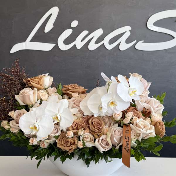 Large arrangement of beige roses and white orchids in a white bowl vase