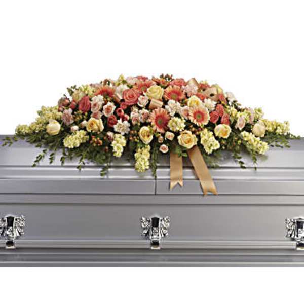 Large floral spray on a silver casket with peach and cream flowers