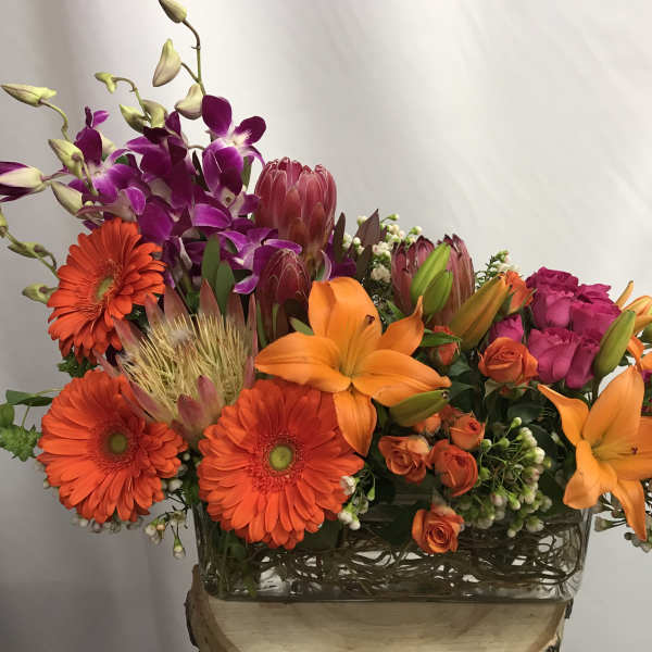 Bright mixed bouquet with orange lilies, gerbera daisies, and purple orchids in a glass vase