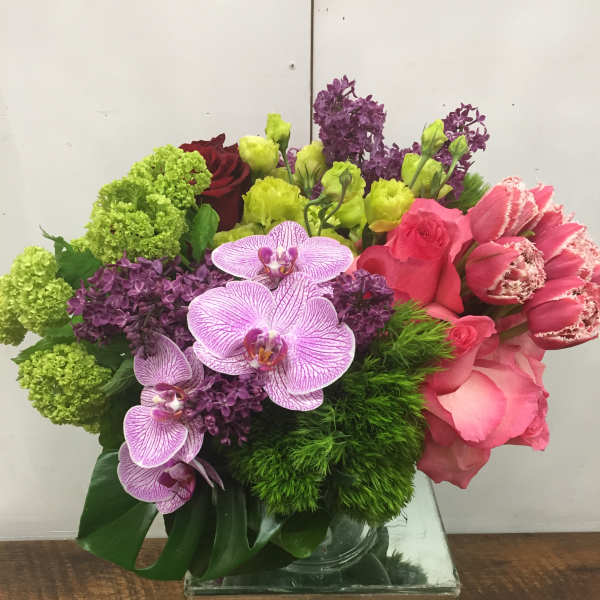 Colorful bouquet of orchids, roses, and carnations in a clear glass cube vase