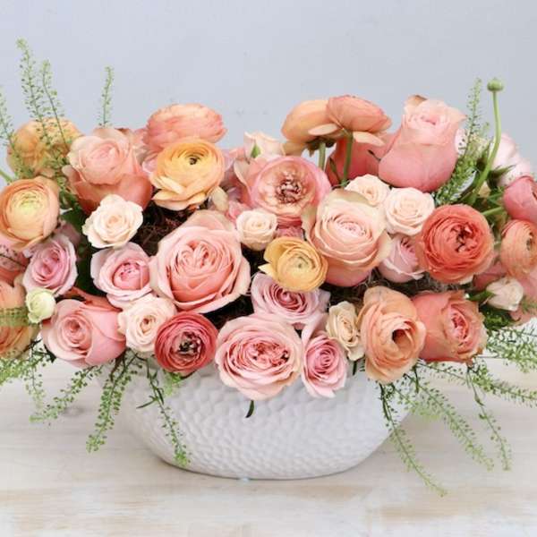 Low centerpiece of peach and pink roses and ranunculus in a white ceramic bowl