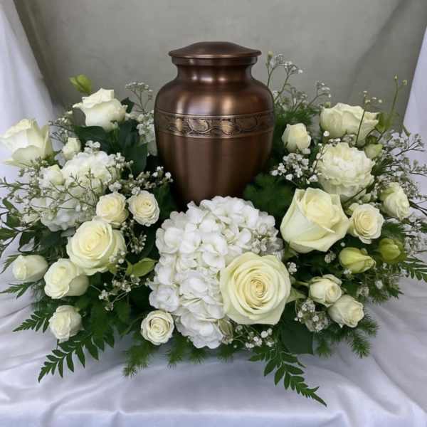 White roses and hydrangeas arranged around a bronze urn.