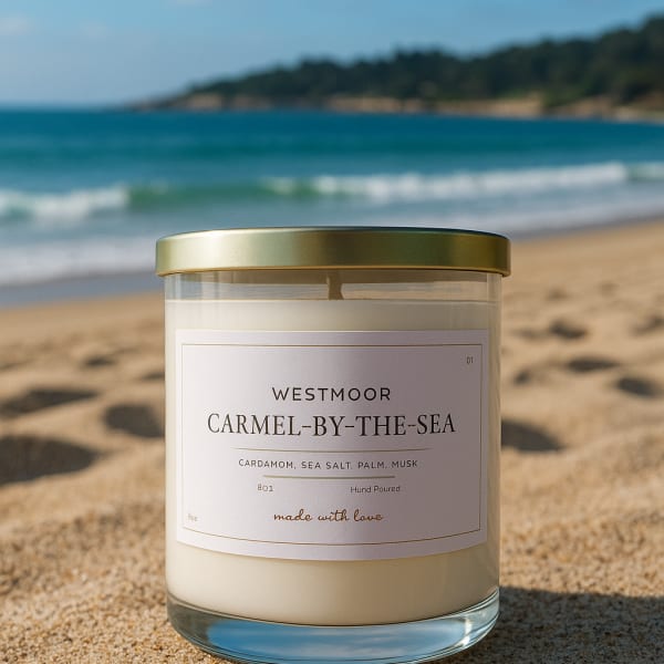 A scented candle in a glass jar with a gold lid on a sandy beach