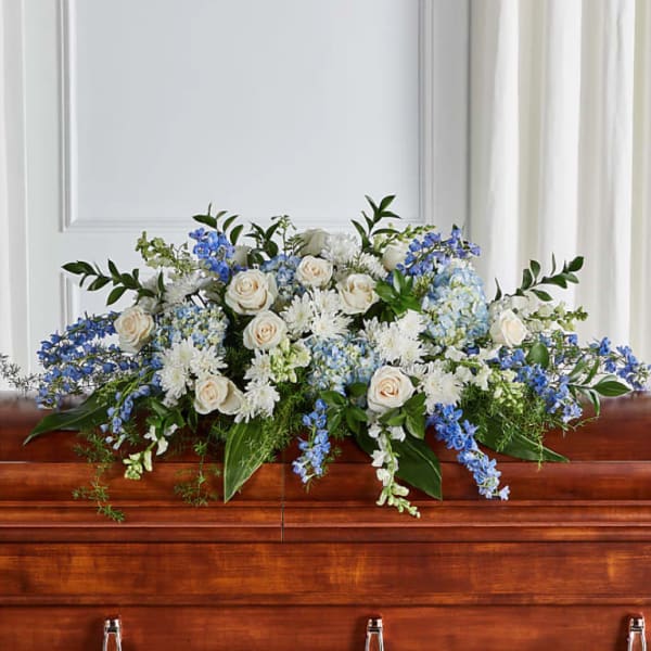 White and blue casket spray with roses and delphinium on a wooden casket