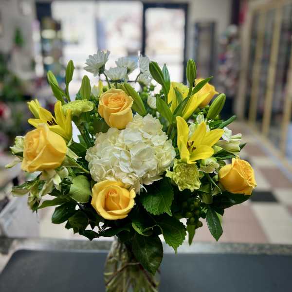 Yellow roses and lilies arranged with white hydrangea in a glass vase