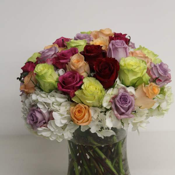 Low dome of multicolor roses with white hydrangeas in a clear glass vase