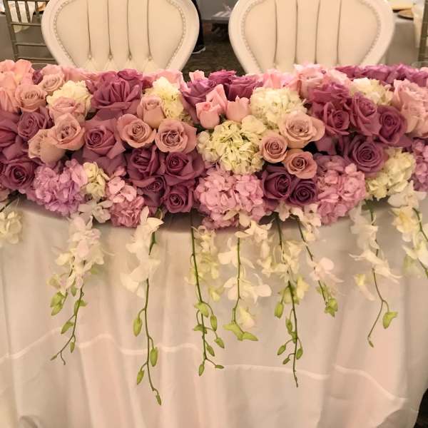 Large floral table arrangement with pink and purple roses and hanging white orchids