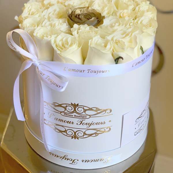 Round white box filled with cream roses and a single gold rose, tied with a white ribbon.