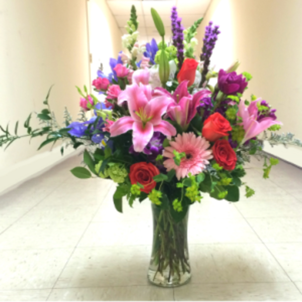Tall mixed bouquet of pink lilies, roses, and purple flowers in a glass vase