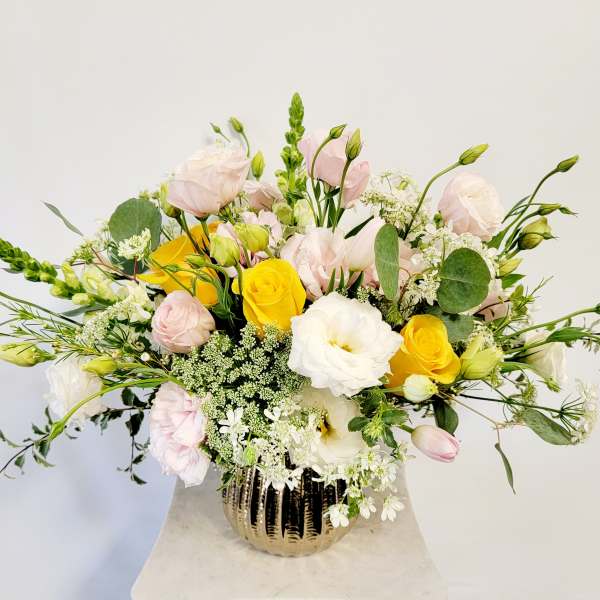 Mixed bouquet of yellow, white, and pale pink flowers in a gold vase