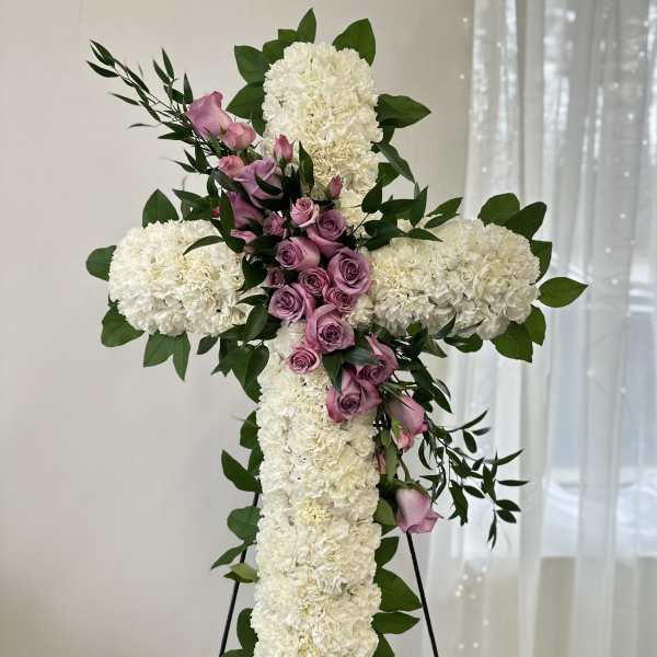 White floral cross with pink roses and greenery on a stand