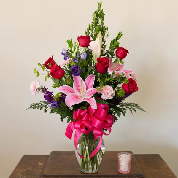 Mixed bouquet of pink lilies, red roses, and purple flowers in a glass vase
