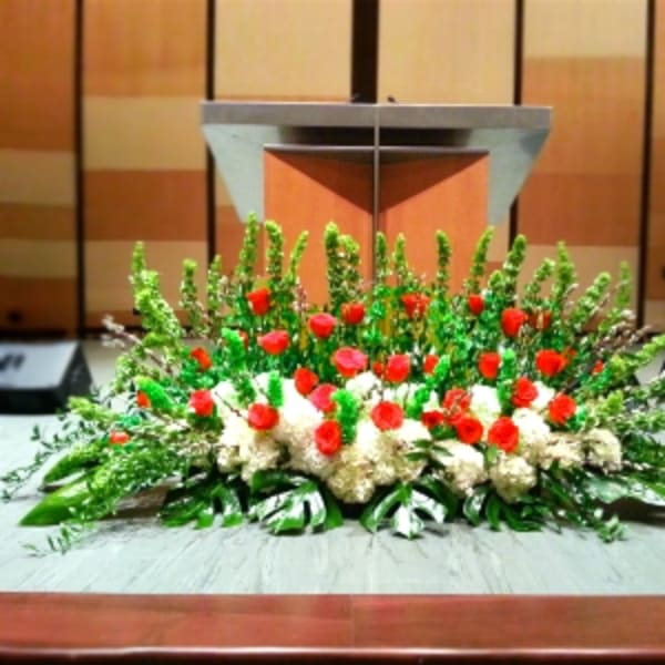 Large altar spray with red roses, white hydrangeas, and tall green spikes in front of a podium