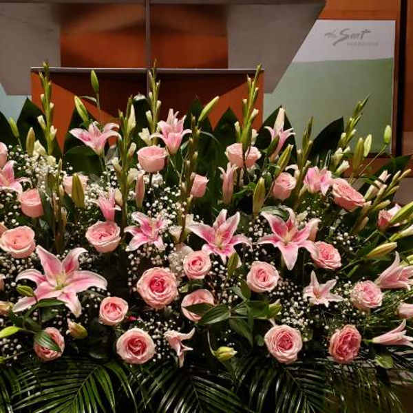 Large low arrangement of pink roses, pink lilies, and white filler flowers in front of a stage.