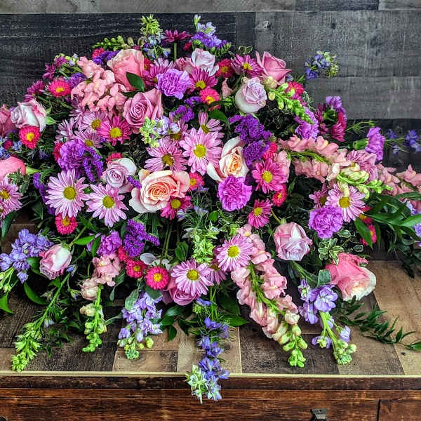 Low spray of pink and purple roses, mums, and snapdragons arranged in a wide mound.