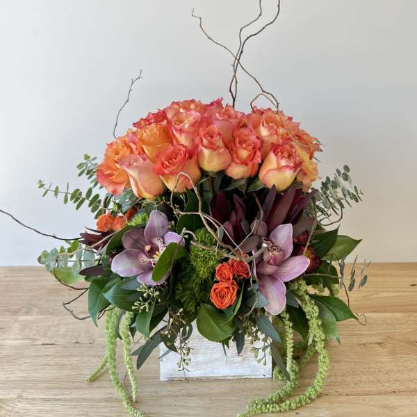 Orange roses and purple orchids in a white box with curly branches