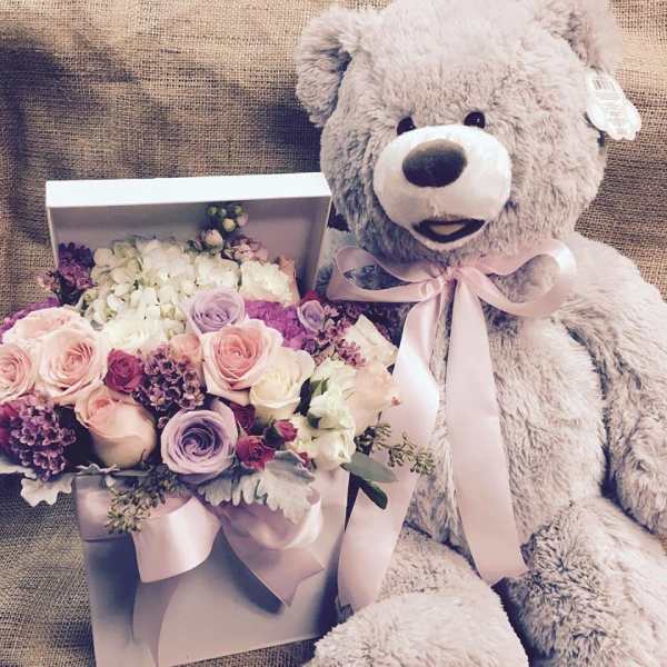 Bouquet of pastel roses and hydrangeas beside a teddy bear