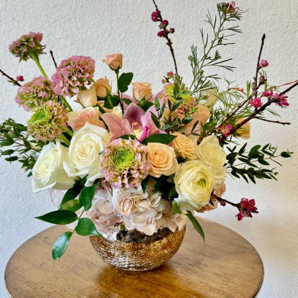 Mixed bouquet of roses, hydrangea, and orchids in a gold bowl vase