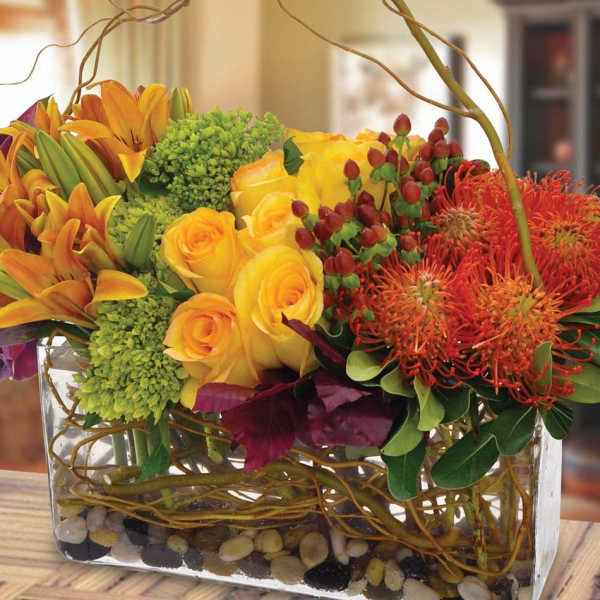 Yellow roses and orange lilies in a glass vase with red blooms