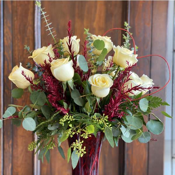 Cream roses in a tall red vase with burgundy accents