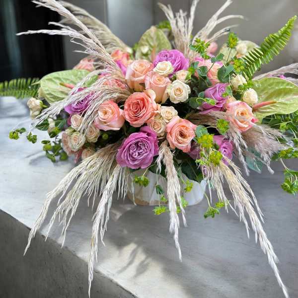 Low arrangement of pink and peach roses with pampas grass in a white container