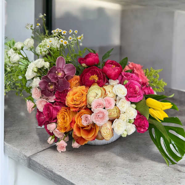 Mixed bouquet of roses, peonies, and orchids in a white bowl vase