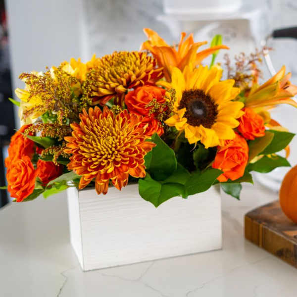 Orange and yellow autumn bouquet in a white box beside a small pumpkin