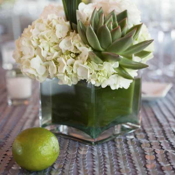 Low white hydrangea and green succulent arrangement in a glass cube vase on a table