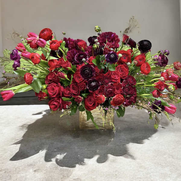 Large red and burgundy floral arrangement in a gold rectangular vase