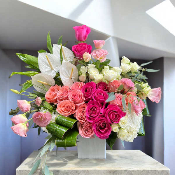Pink and white floral arrangement with roses and anthuriums in a white vase