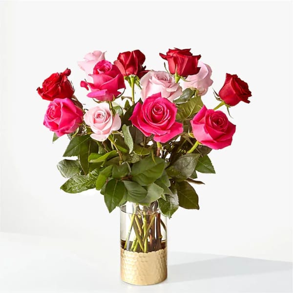 Mixed red and pink roses arranged in a clear glass vase with a gold base