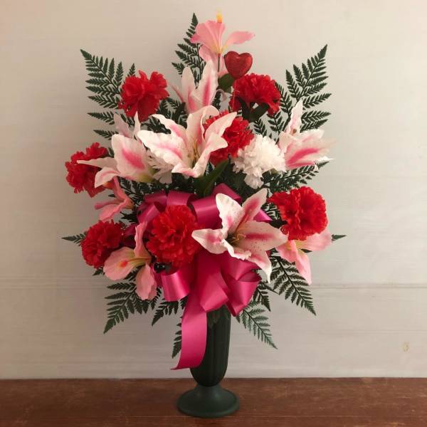 Tall arrangement of red carnations and pink-white lilies in a dark green vase with a pink bow.
