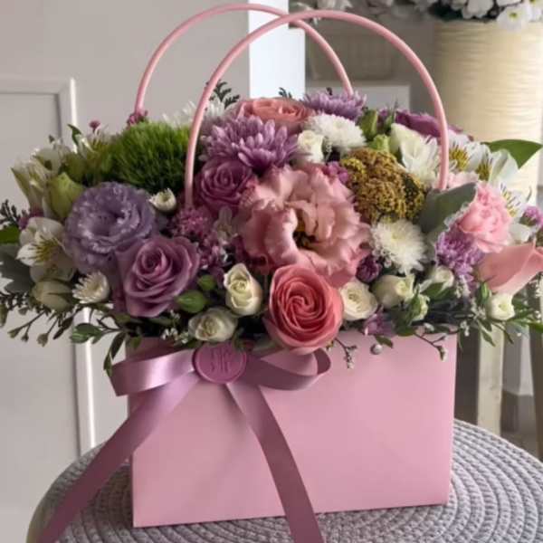 Pink floral arrangement in a pink gift box with ribbon handles