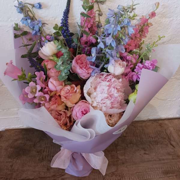 Pastel bouquet of pink, blue, and peach flowers wrapped in lavender paper