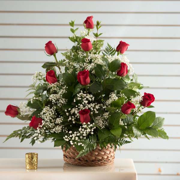 Basket arrangement of red roses and white filler flowers in a woven basket.