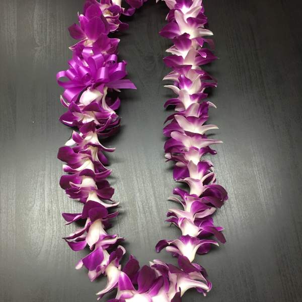 Purple and white orchid lei on a dark surface