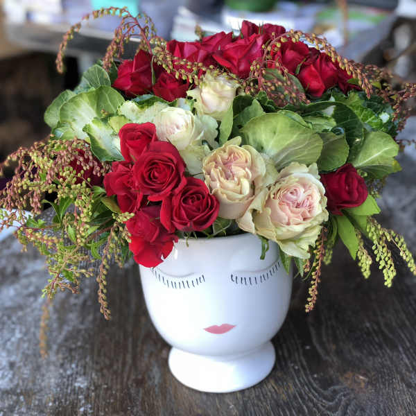Red and blush roses arranged in a white face-shaped vase