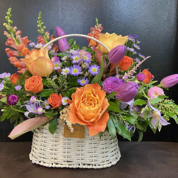 Basket arrangement with orange and purple flowers