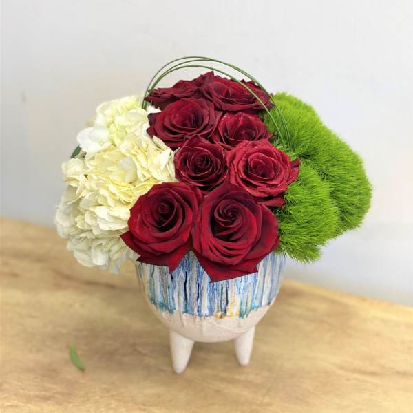 Red roses with white hydrangea and green moss in a decorative vase